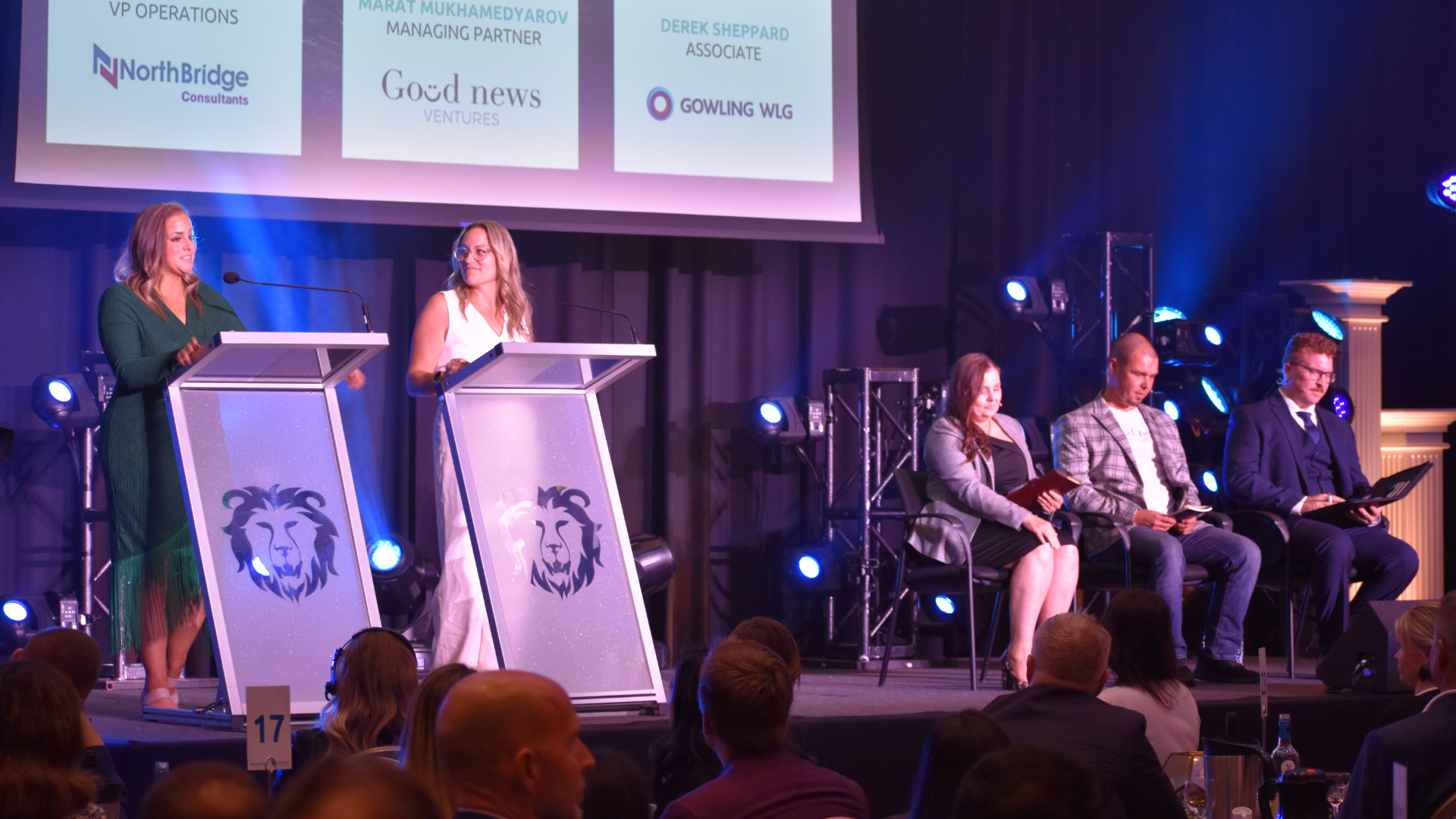 Two speakers and a panel of judges are seen on stage