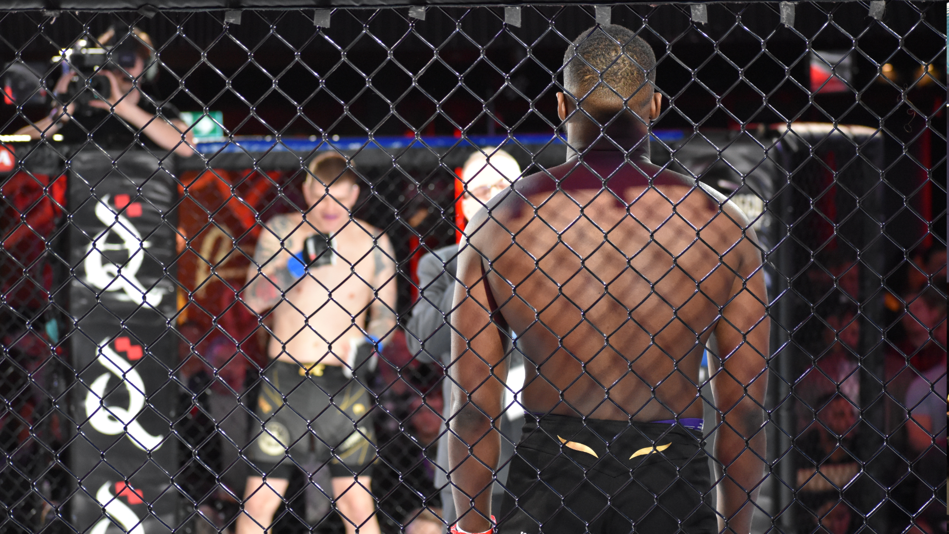 Two fighters are shot by a cameraman at the top of an MMA cage